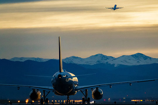 An airplane on the tarmac at sunset with mountains in the background.