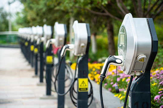 A set of silver electric vehicle chargers against a backdrop of green grass and yellow flowers.