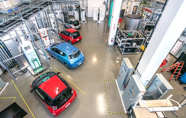 Photo of four cars parked at electric vehicle chargers in laboratory setting.