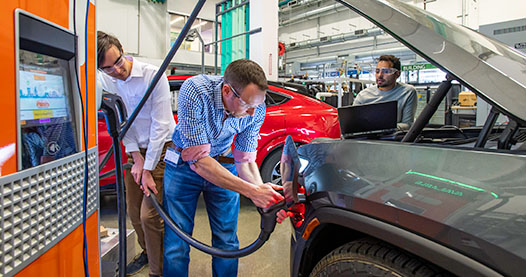 Three researchers working on an electric vehicle's charging port.