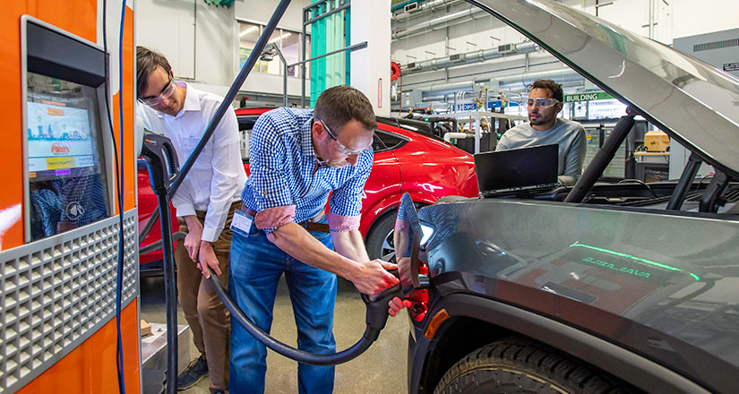 Three researchers looking at an electric car's charging port.