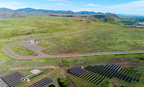 Aerial photo of solar panels and road atop a mesa with mountains in background.
