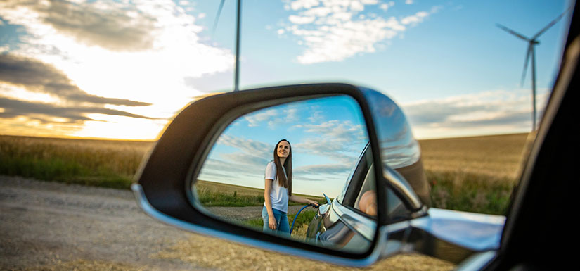 A car mirror with a woman's reflection with wind turbines and a rural setting in the background.
