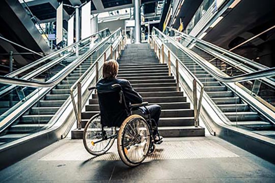 A person in a wheelchair looking up from the bottom of a staircase.