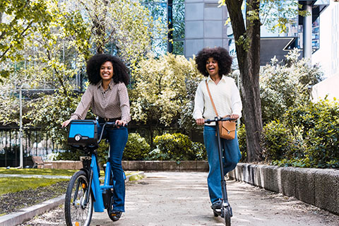 Two wommen riding electric micromobility in a park.