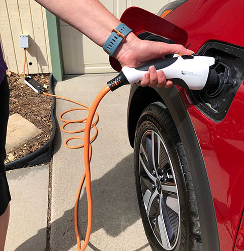 A hand plugging a charger into a red EV.