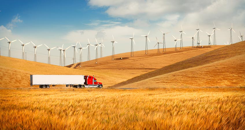 Truck going in the countryside with wind farm on the hills.