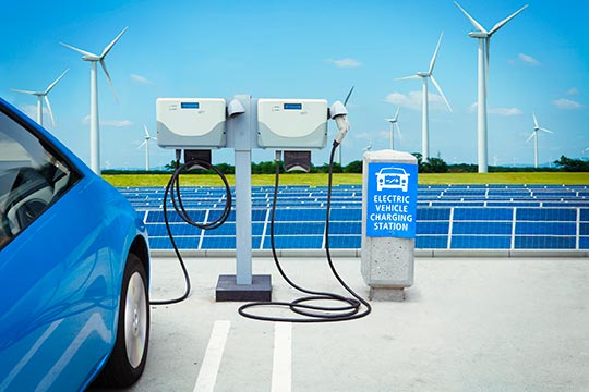 An electric car charging next to a row of wind turbines and solar panels