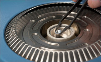 Photo of tweezers placing a small round battery cell in the center of a piece of scientific equipment (differential scanning calorimeter).