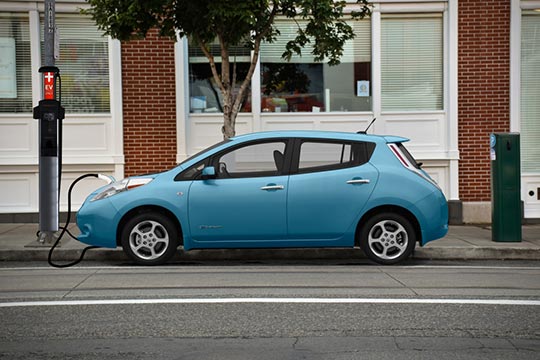 A Nissan Leaf charges its battery with an electric charging station attached to a streetlight