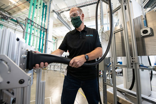 Photo of a person wearing a mask in a lab and holding a fueling hose.