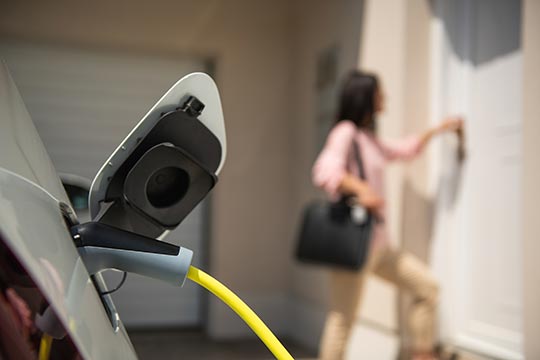 A woman walks into her home after plugging in her electric vehicle to charge.