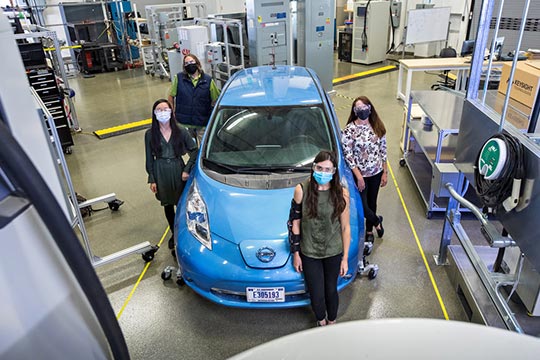 Four women standing around an electric vehicle in a lab.