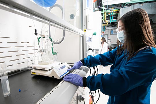 A scientist uses equipment sitting inside a laboratory fume hood.
