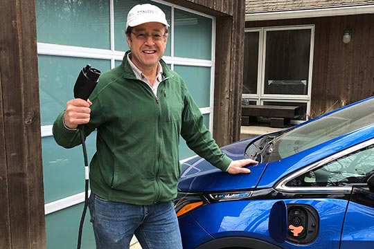 A man holds a charging cable while standing next to an electric vehicle.
