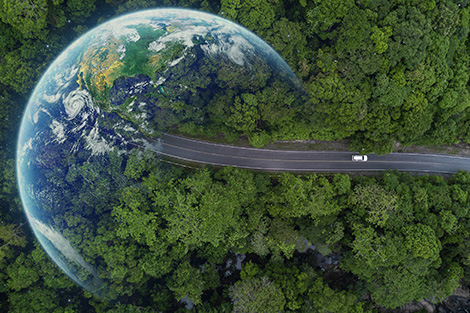 Aerial image of a car driving on pavement through a heavily wooded area toward the planet Earth faded on the left.