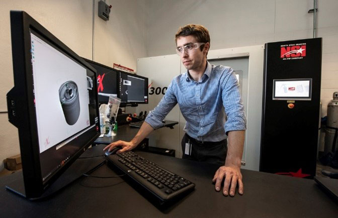 A researcher stands in front of a computer with an X-ray image of a battery on the screen.