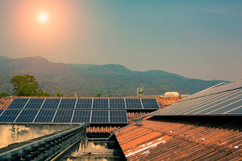 Photo showing solar panels on an orange roof with the mountains and the sun in the background.