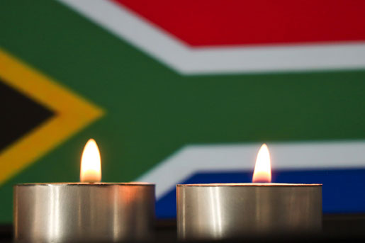 Two burning votive candles in front of a South Africa flag.