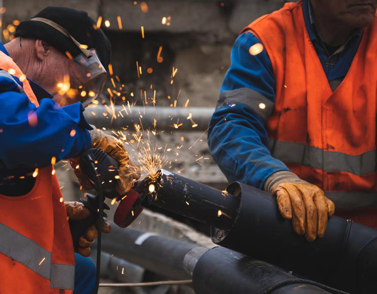 Two men welding a pipe while sparks fly in the air.