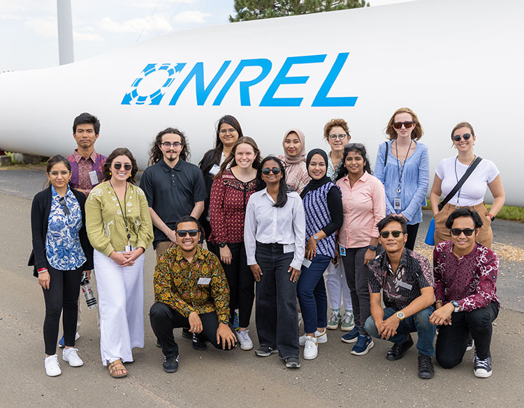 A group of people stands in front of a large NREL logo.