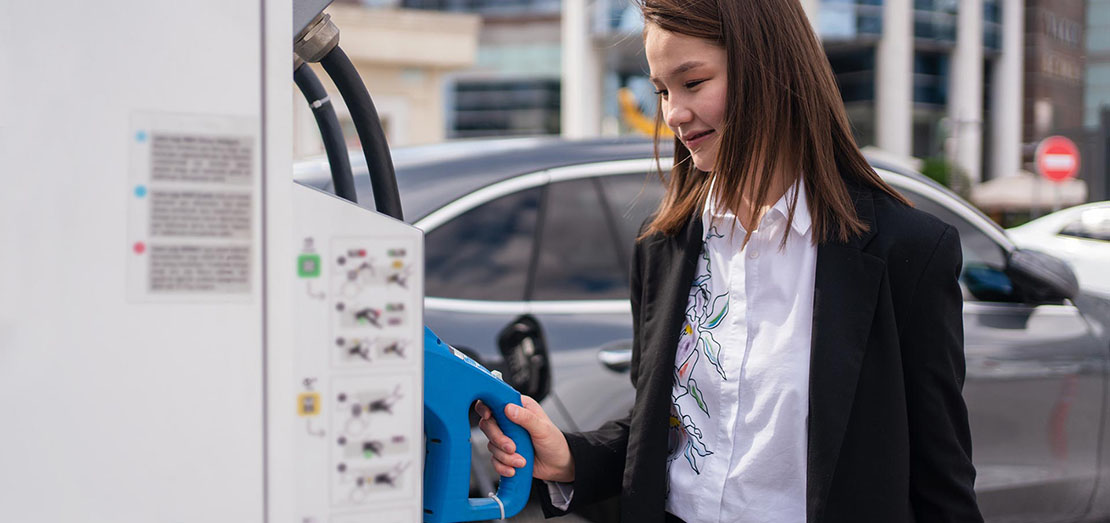 Young woman charging an electric car at public charging station