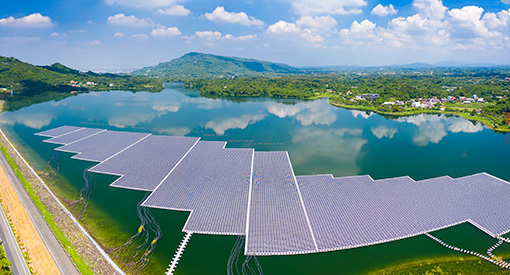 A large solar PV installation floating on a body of water with lush green landscape and hills in the background.