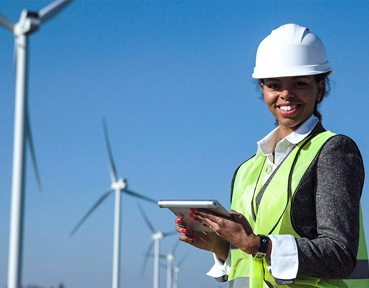 A woman in a hard hat and safety vest in front of wind turbines