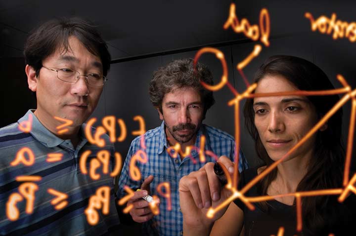 Photo of scientists drawing models on a clear marker board.
