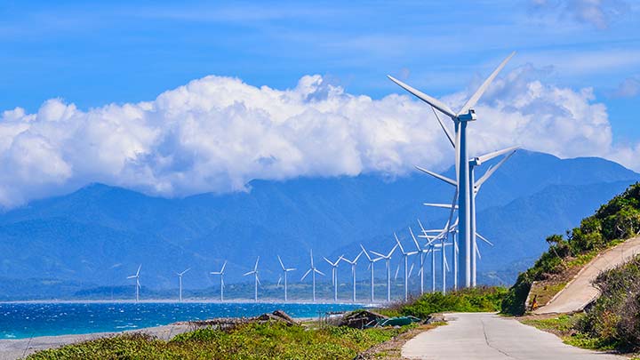 Wind turbines along a coast with mountains in the background.
