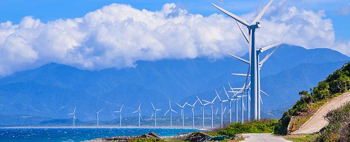 A wind farm along a shoreline in the Philippines, with mountains in the background.