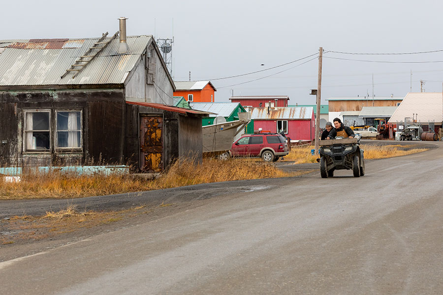 Person drives quad down dirt road in rural Alaskan community.