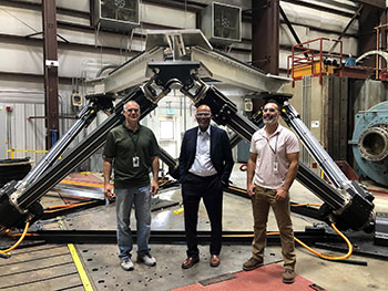 Three researchers standing in front of a large-amplitude motion platform at NREL's Flatirons Campus.