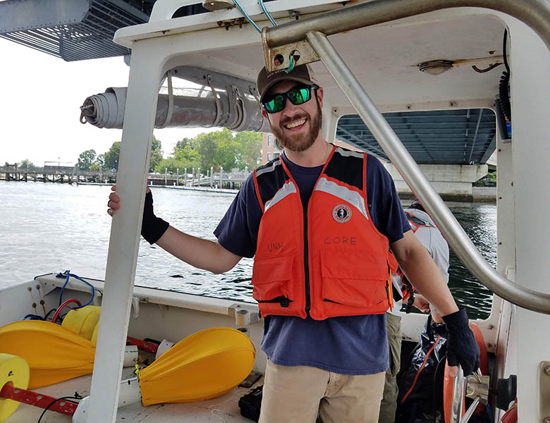 Patrick standing on a boat beneath a bridge in a life vest, sunglasses, and baseball hat.