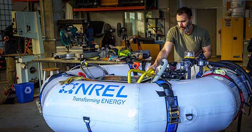 A researcher works on a device in an inner tube labeled with NREL's logo in a lab.
