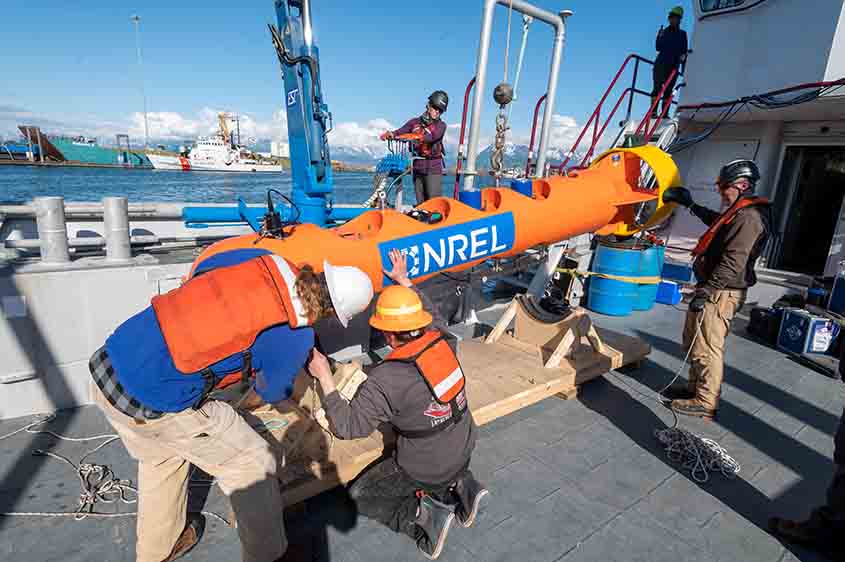 Four people in hard hats on a dock adjust a buoy bearing the NREL logo