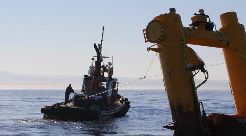A boat towing a wave energy conversion device at sea.