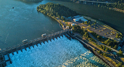 A dam crossing half a river as viewed from above with a power station on an island in the middle of the river.