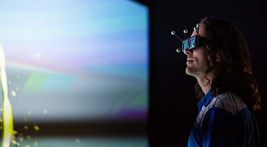 A man with special goggles reviews visualized data on a wall-size screen.