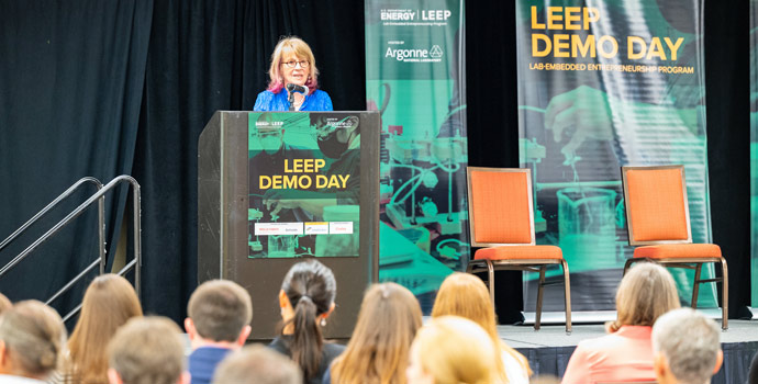Person standing on a stage behind a podium, both bearing signs reading, 'LEEP Demo Day'.