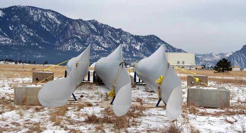 Three wind turbine blades as viewed from their tips propped up side by side in a snowy field in front of mountains