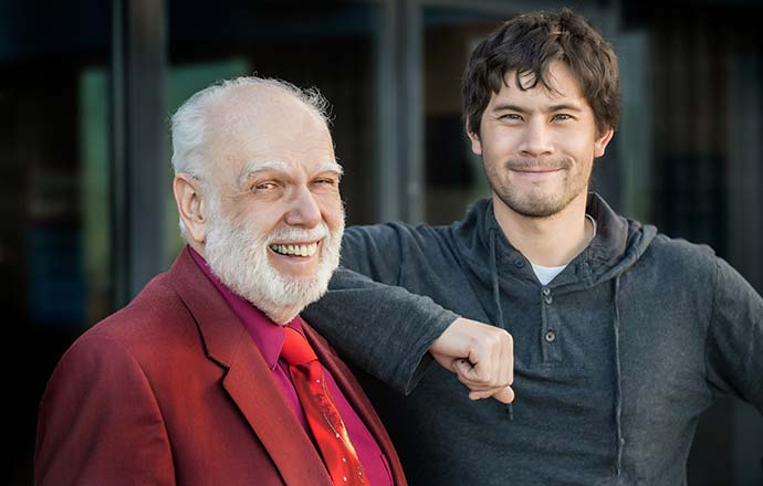 A smiling man in a red suit stands with one of his students.
