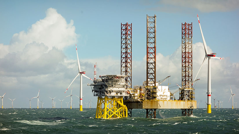 A construction platform in front of several offshore wind turbines in open water.