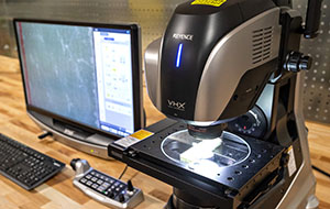 A computer monitor sits next to a microscope on a desktop.