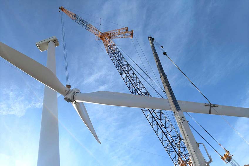 A crane lowers a rotor removed from a wind turbine.
