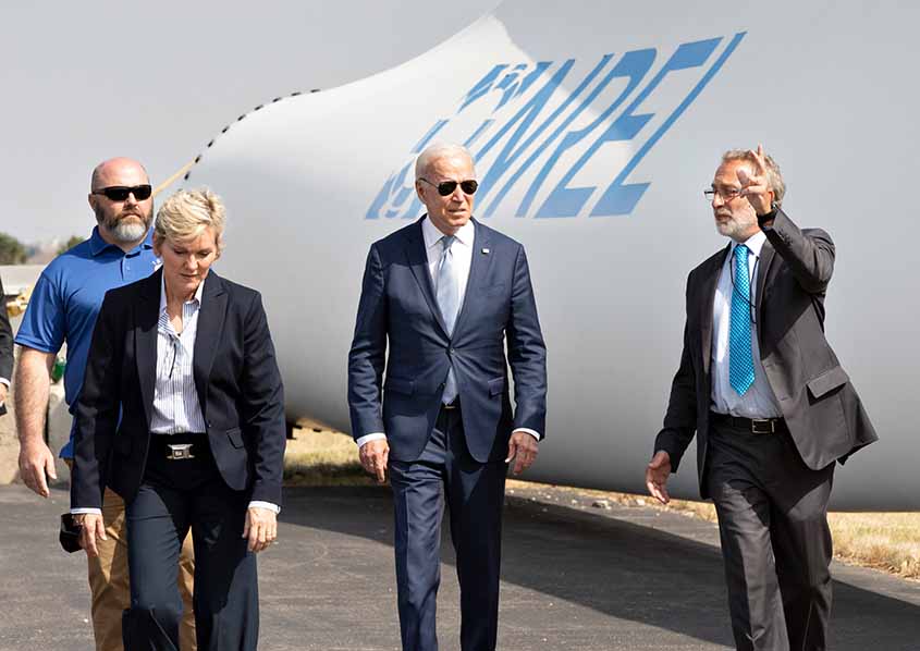 Passing in front of a wind turbine blade stamped with NREL's logo, President Biden walks with Martin Keller and Jennifer Granholm