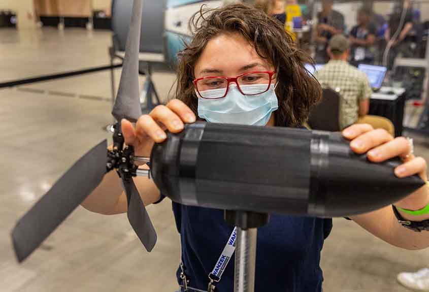 A woman in glasses and a surgical mask shifts a model wind turbine.