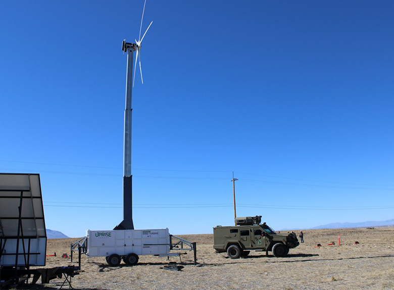 A military jeep parked beside a mobile wind turbine in a remote area.