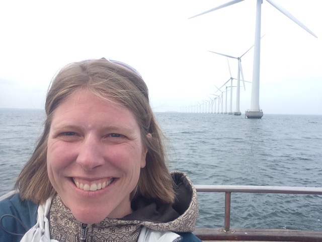 Kendra Ryan smiling in front of a long row of offshore wind turbines.