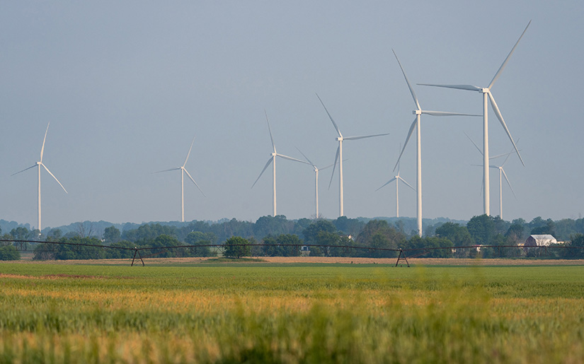 Wind turbines behind an irrigation system in a crop field. 